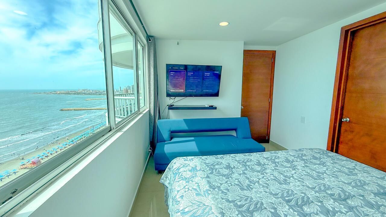 A room with a bed, a TV, and a window overlooking the beach.