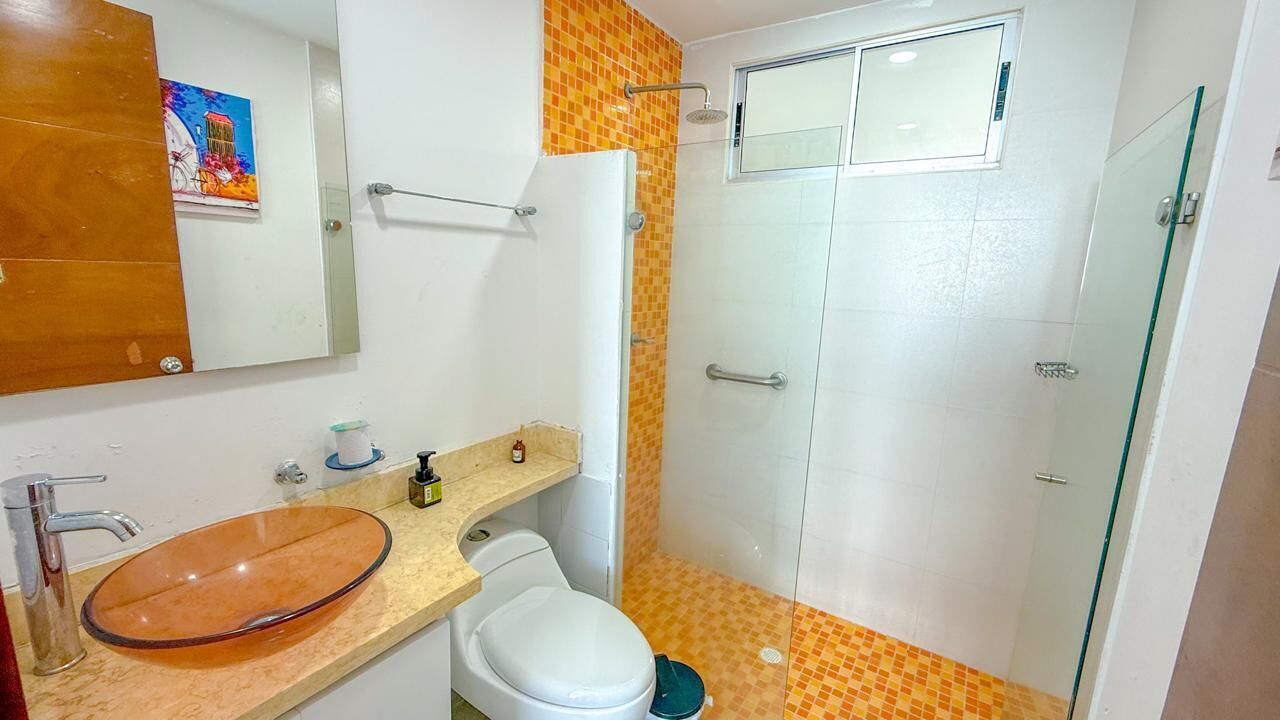 A bathroom with a glass sink, white toilet, and a glass shower enclosure.