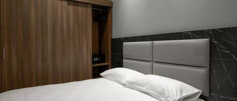 A bedroom with a bed, a wooden wardrobe, a marble headboard, and a bedside table with a remote control.