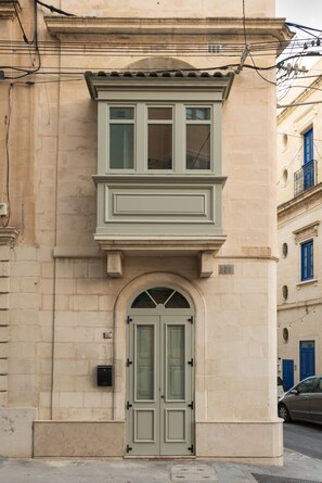 Un edificio con fachada de color claro, un arco central en la entrada y una ventana encima.