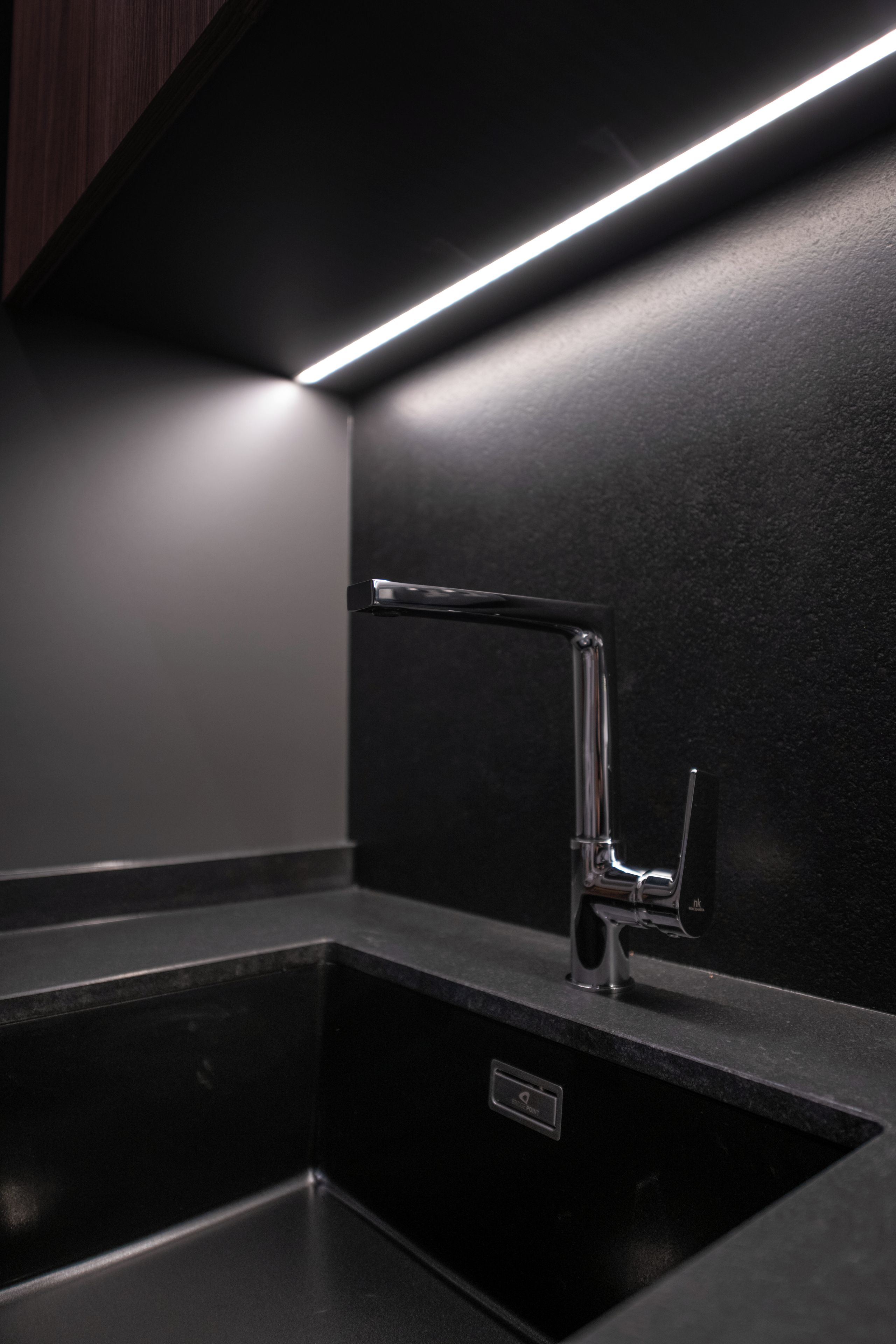 Une cuisine moderne dotée d’un robinet élégant, d’un plan de travail noir et d’un éclairage sous les meubles hauts.