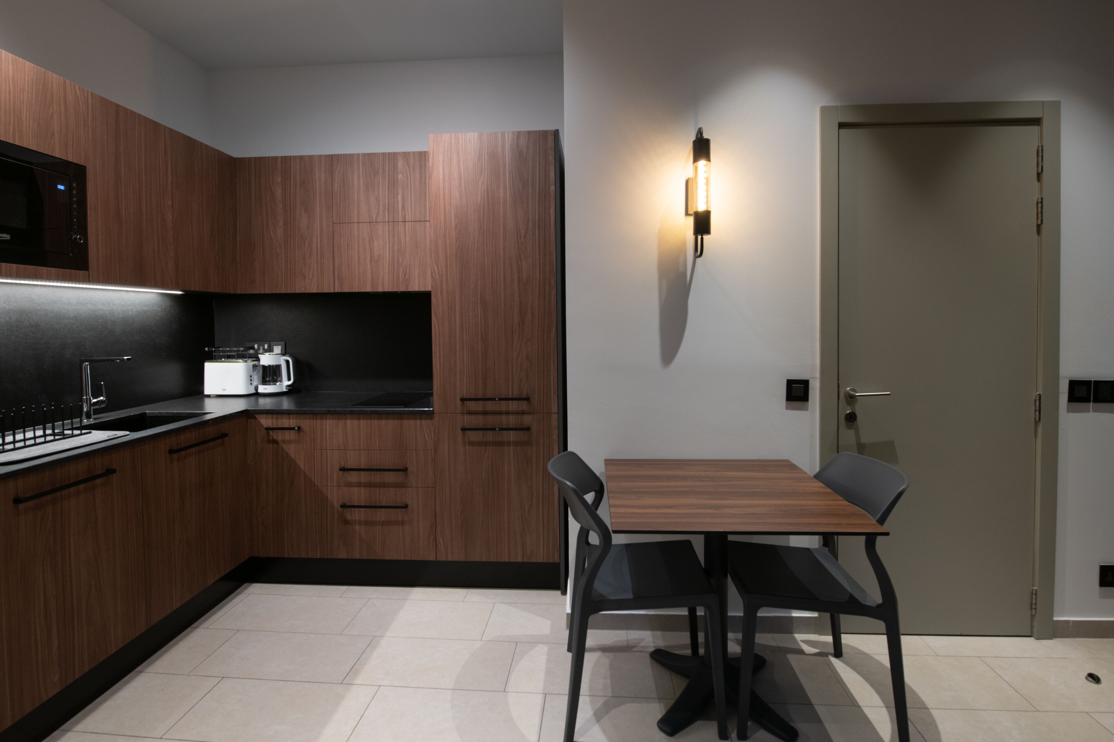 Une cuisine moderne avec des meubles en bois, un plan de travail noir, un micro-ondes blanc et une table à manger avec des chaises.