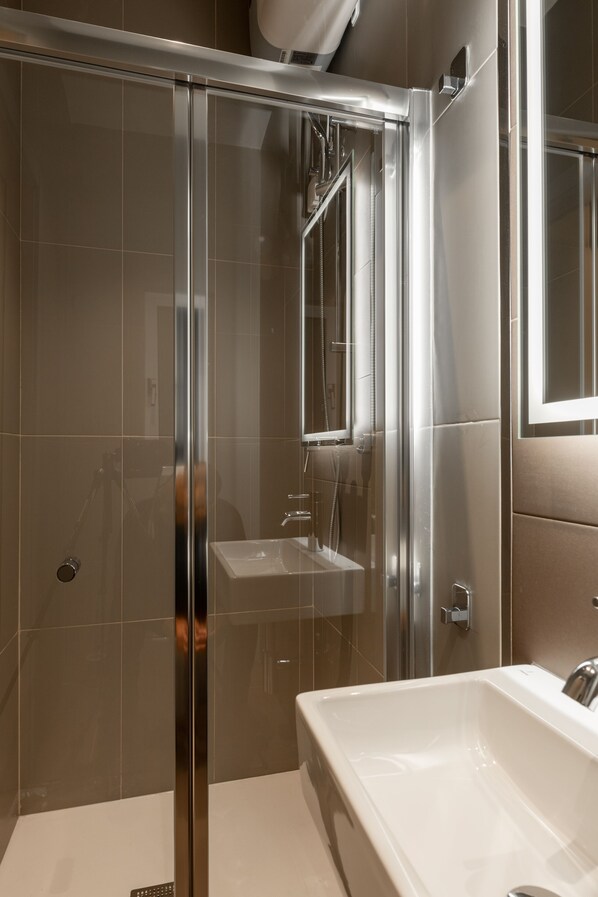 Un baño moderno con ducha envuelta en vidrio, un lavabo blanco y un espejo grande.