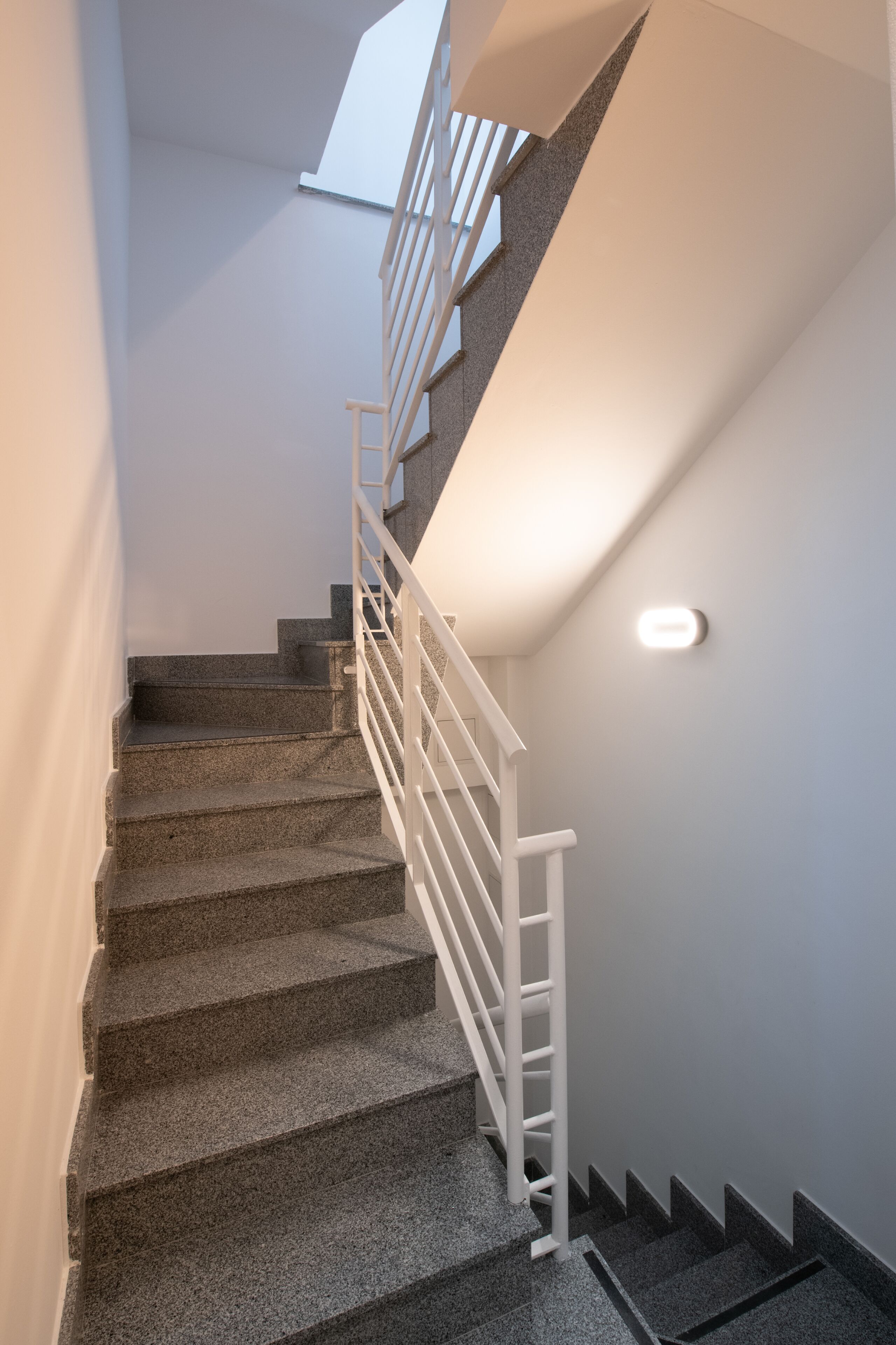 Una escalera de granito con barandales blancos que conduce a un piso superior.