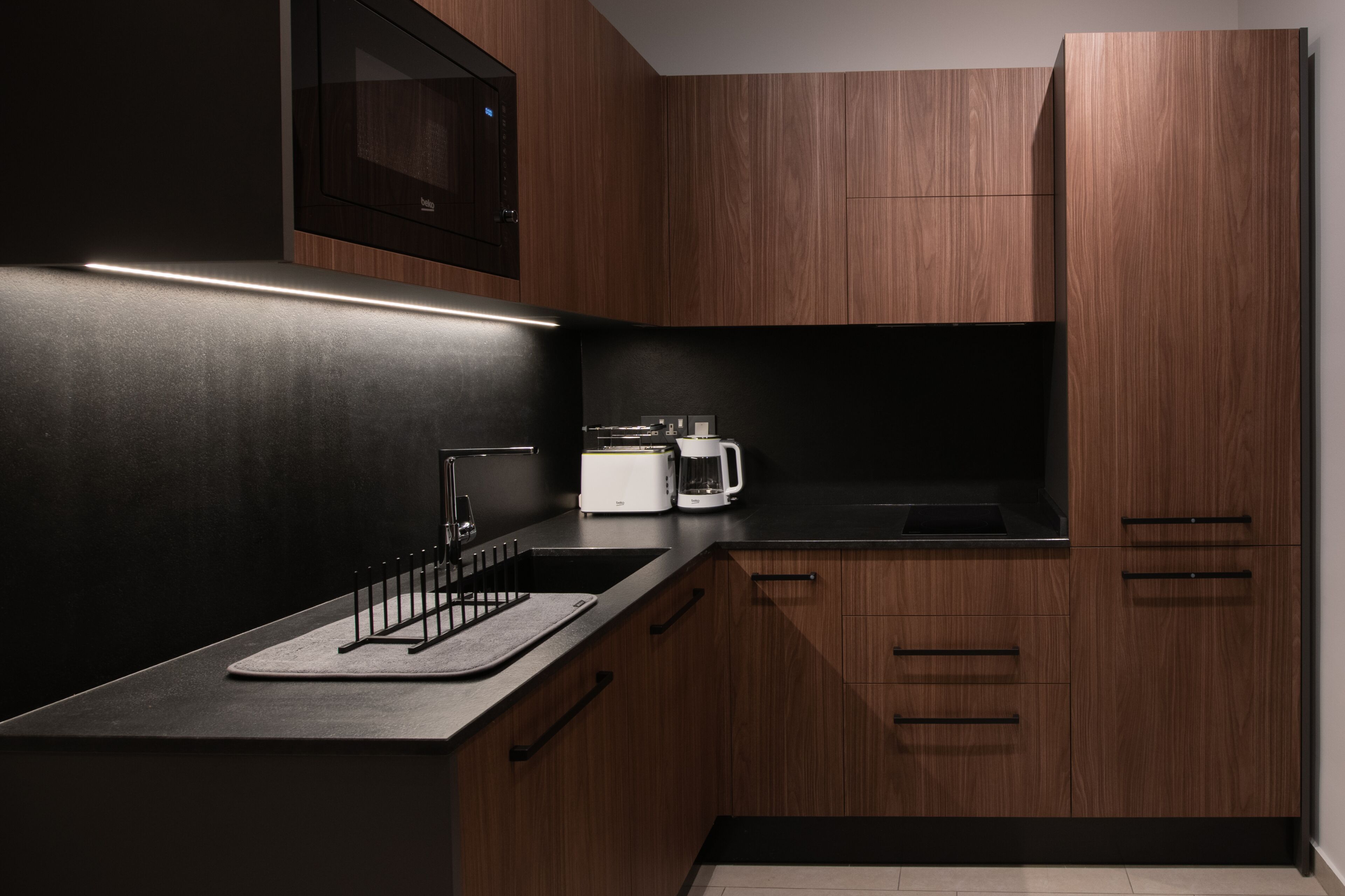 Une cuisine moderne avec des meubles de rangement aux couleurs sombres, un plan de travail noir et un four à micro-ondes encastré.
