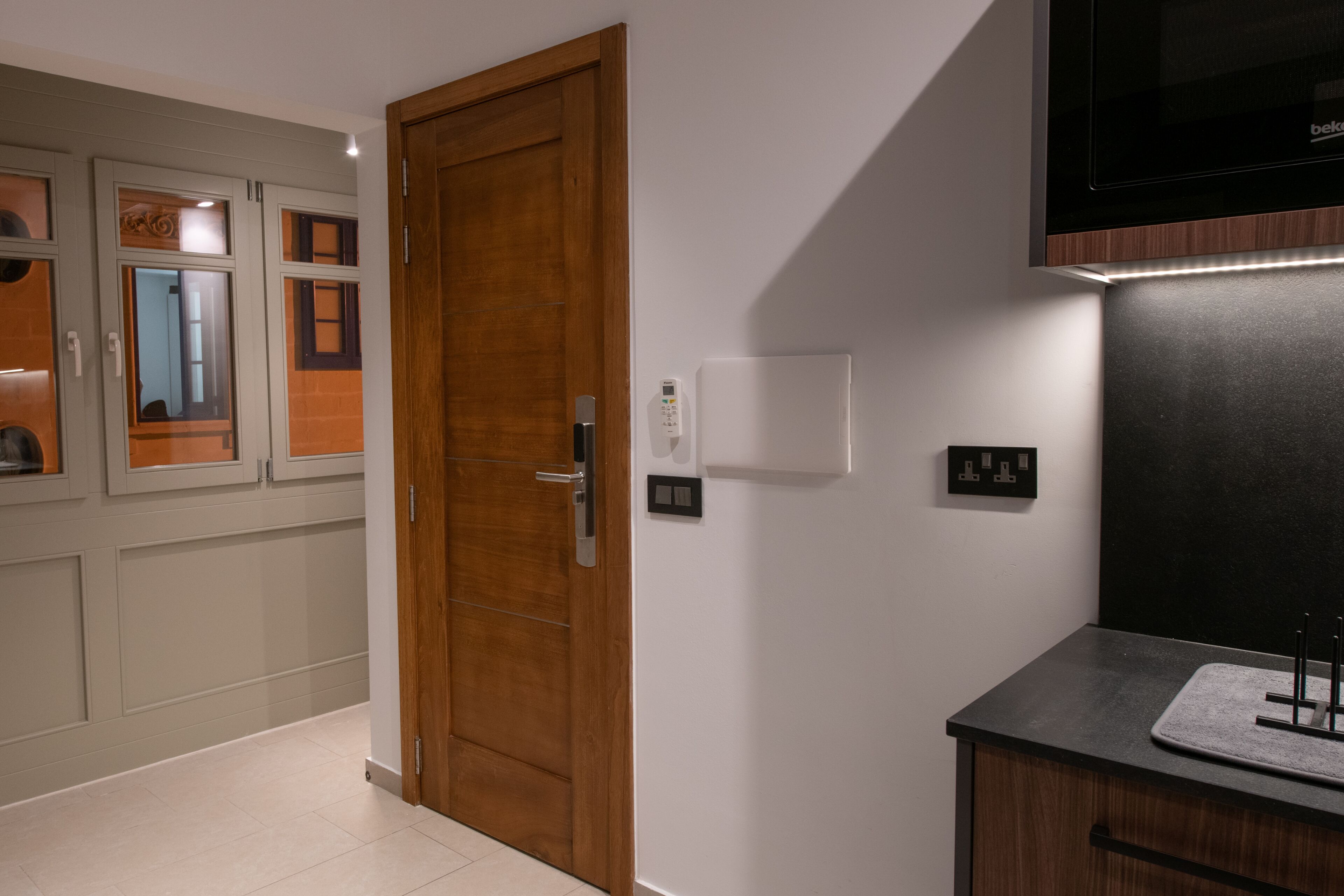 Un couloir avec une porte en bois, un interrupteur fixé au mur et un comptoir noir avec un évier.