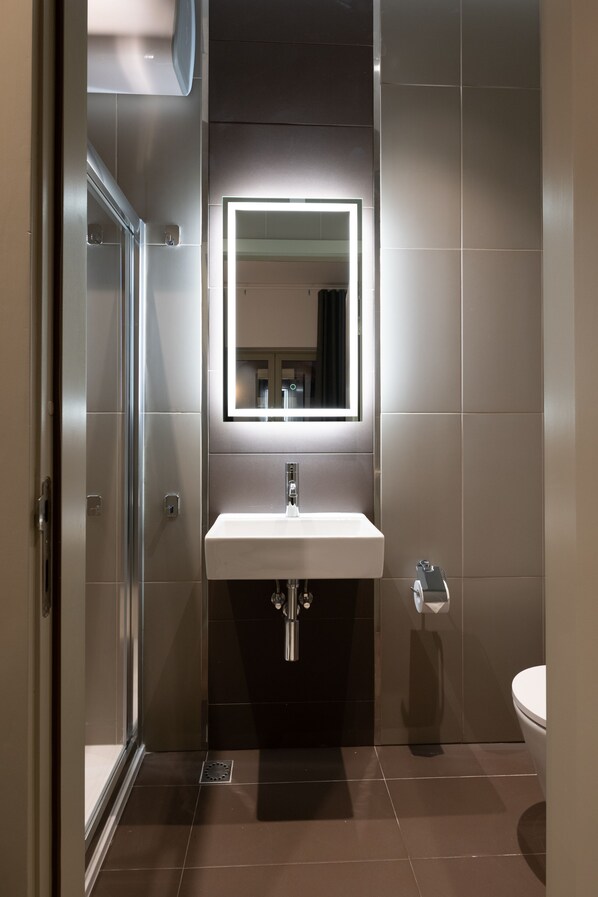 Un baño moderno con cabina de ducha de vidrio, un lavamanos blanco con espejo y un inodoro.