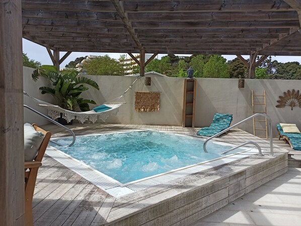 Een houten terras met een jacuzzi, een hangmat en loungestoelen.