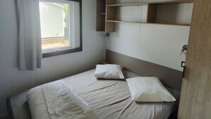 Een enkel bed met twee kussens, een raam met gordijnen en een houten plankunit.