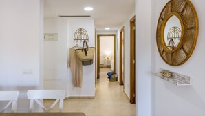 Un couloir avec un banc blanc, un porte-manteau suspendu, un panier en osier et un miroir fixé au mur.