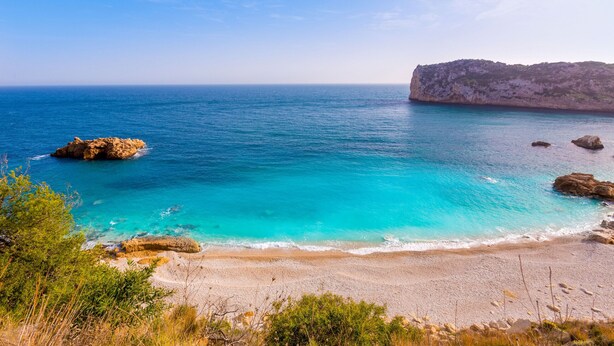 Un paysage côtier caractérisé par une eau d’un bleu limpide, des affleurements rocheux et une plage de sable.