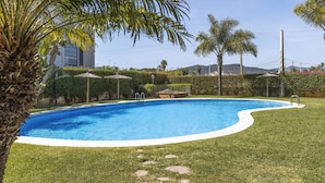 Une piscine à bord incurvé, entourée d’une pelouse bien entretenue et de palmiers.