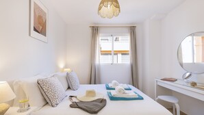 Une chambre d’hôtel avec un lit, un bureau, une chaise, une fenêtre avec des rideaux, un luminaire suspendu et un tableau encadré au mur.