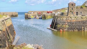A coastal harbor with boats docked at wooden piers, a lighthouse, and a stone building. - Nebo Pod (Rhosgoch)