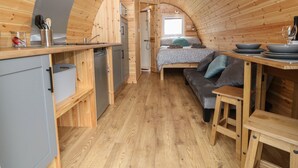 A compact, wooden cabin interior with a kitchenette, a bed, and a dining area. - Nebo Pod (Rhosgoch)