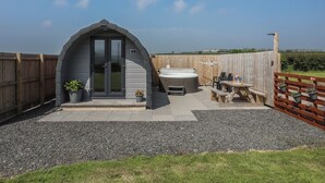 A small, private hot tub area with a covered seating area, a wooden fence, and a gravel patio. - Nebo Pod (Rhosgoch)