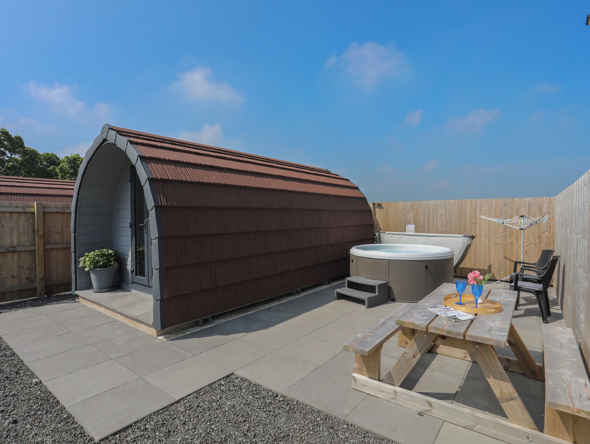 A covered outdoor area with a hot tub, a wooden bench, and a potted plant.
