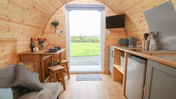 A cozy wooden interior with a sofa, dining table, and kitchen area. - Nebo Pod (Rhosgoch)