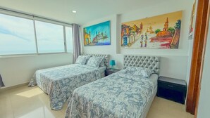 Een hotelkamer met twee bedden, een groot raam en twee schilderijen aan de muur.