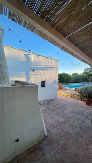 A covered outdoor area with a pool, stone walls, and string lights.