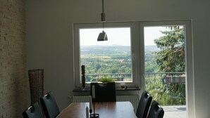 A dining area with a wooden table, two chairs, a candle, and a view of a green landscape through large windows. - Ferienhaus mit Wunderschöner Aussicht in Zentraler Lage (Weitersburg)
