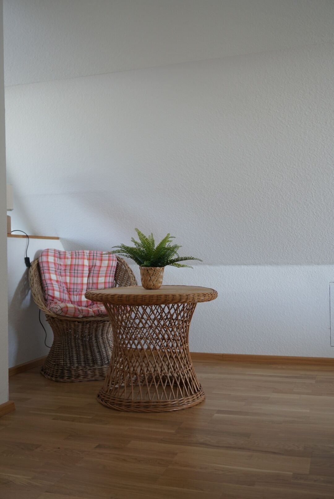 A wicker chair with a plaid cushion and a small table with a potted plant.