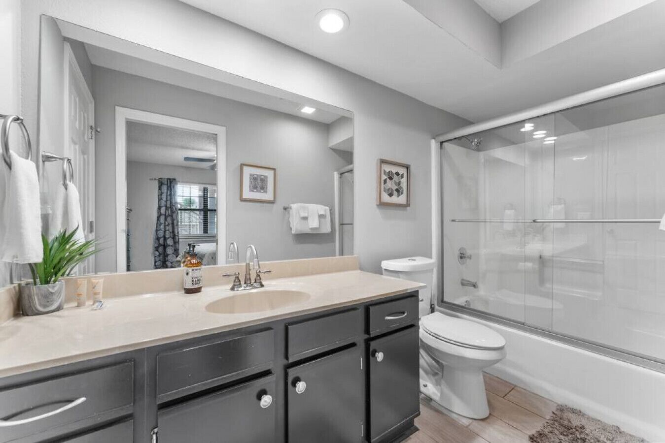 A modern bathroom with a large mirror, a sink, a toilet, and a glass-enclosed shower.