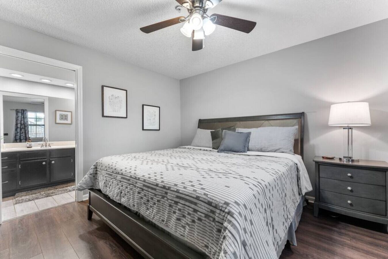 A bedroom with a bed, a nightstand, a ceiling fan, and a bathroom visible through an open door.