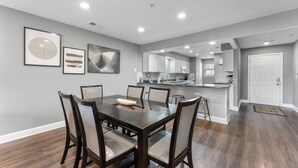 Un'area pranzo moderna con un tavolo e sedie in legno scuro, una cucina sullo sfondo e opere d'arte alle pareti.