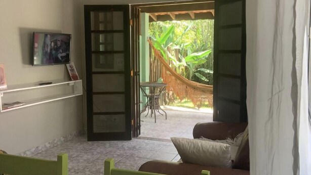 A room with a bed, a TV, a desk, and a view of a hammock and greenery outside.