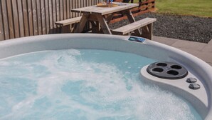 Un bain à remous doté d’un panneau de commande, entouré d’une clôture en bois, d’un banc en bois et d’une zone herbeuse.