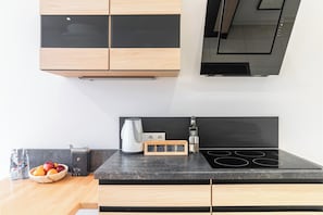 A kitchen with a black countertop, wooden cabinets, a built-in stove, a kettle, and a fruit bowl.