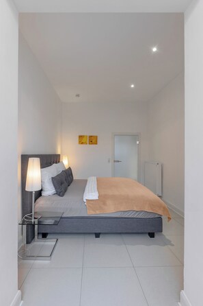A modern bedroom with a bed, bedside lamps, a radiator, and a door.