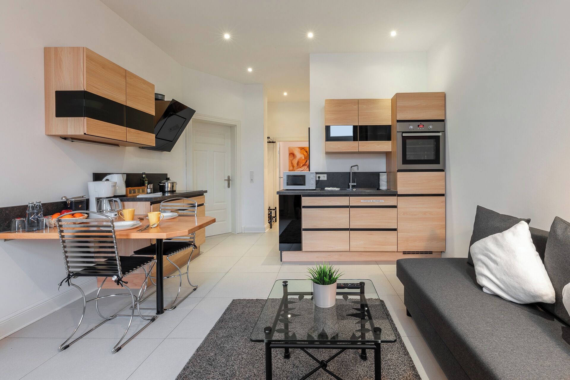 Eine moderne Küche mit integrierten Geräten, eine Essecke mit einer Bank und ein Wohnbereich mit Sofa und Couchtisch.