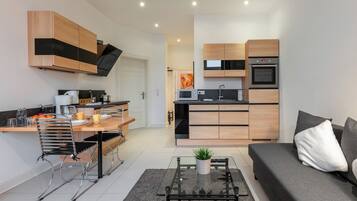 Eine moderne Küche mit integrierten Geräten, eine Essecke mit einer Bank und ein Wohnbereich mit Sofa und Couchtisch.