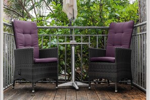 Two wicker chairs with purple cushions and a small metal table on a wooden deck.