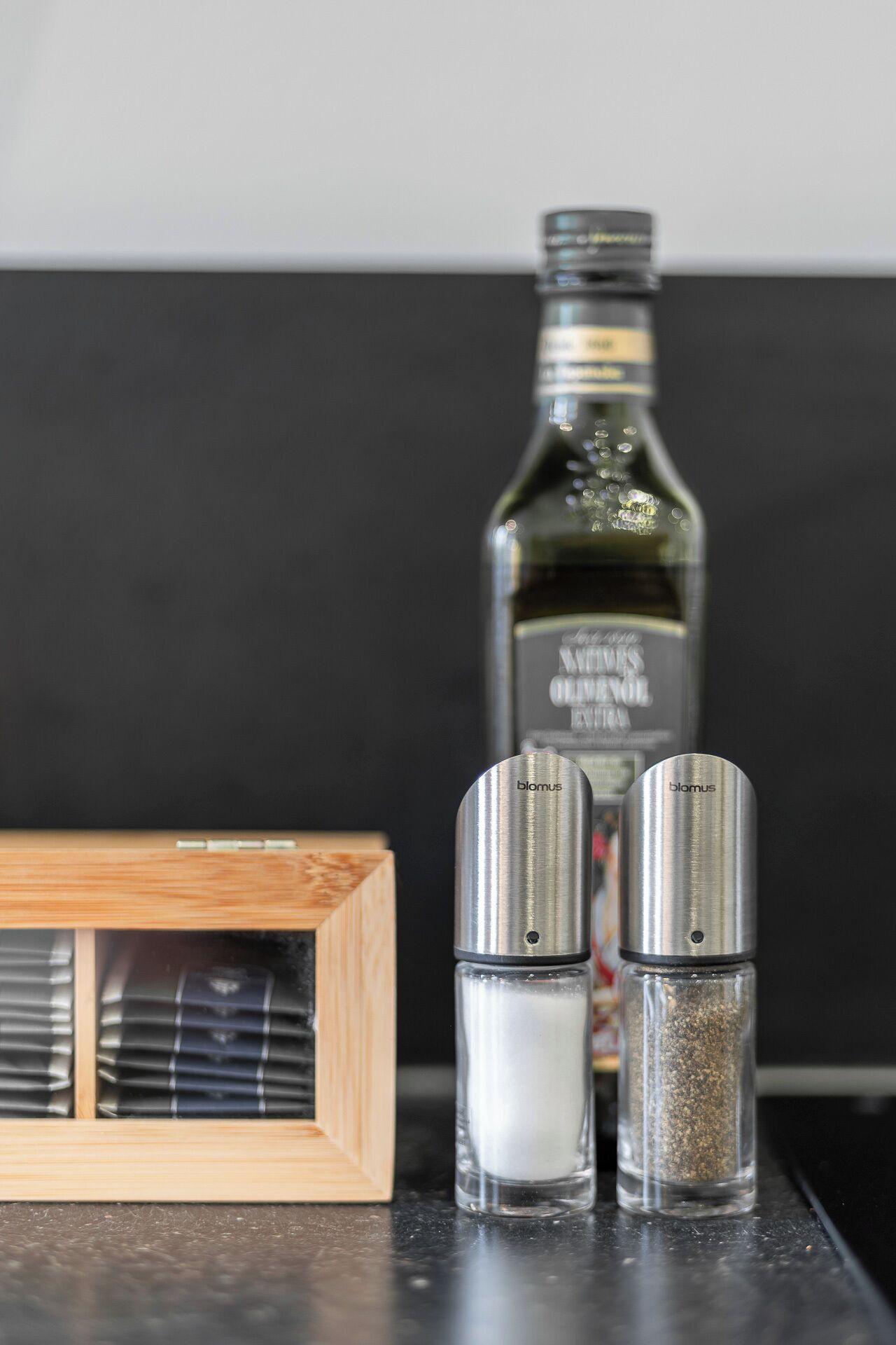 Eine Küchenarbeitsplatte mit einer Olivenölflasche, zwei Salzstreuern und einer Holzkiste.