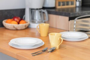 Un comptoir de cuisine avec des assiettes blanches, une tasse jaune et un saladier rempli de fruits.