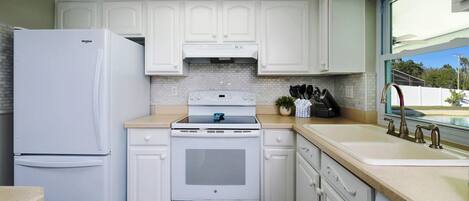 Una cocina con armarios blancos, un refrigerador, una estufa y un lavabo con grifo.