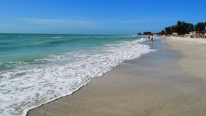 Een strand met golven, mensen en een heldere lucht.