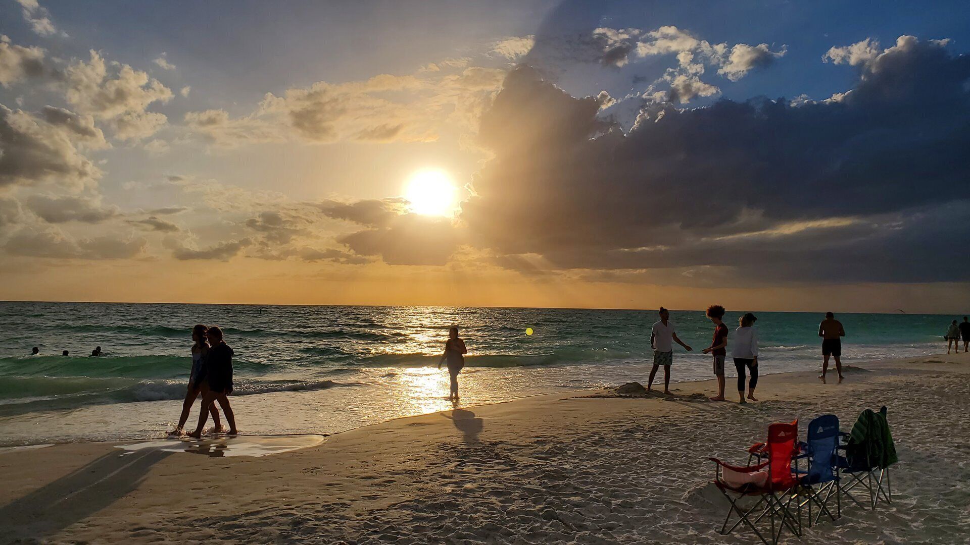 A beach scene with people walking and standing, and a row of beach chairs.