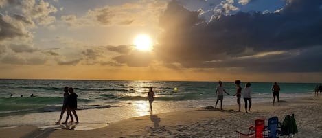 A beach scene with people walking and standing, and a row of beach chairs.