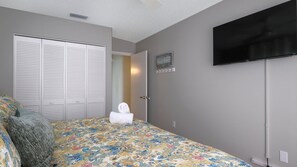 Ein Schlafzimmer mit Bett, Schrank, Fernseher und einer Tür zu einem anderen Raum.