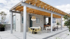 Ein Außenbereich mit Terrasse, ausgestattet mit einem runden Tisch und Stühlen, einer Holzpergola und Blick auf die Stadt.