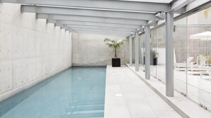 Ein überdachter Schwimmteich mit großen Glaswänden, einem Betonboden und einer Zimmerpflanze in der Mitte.