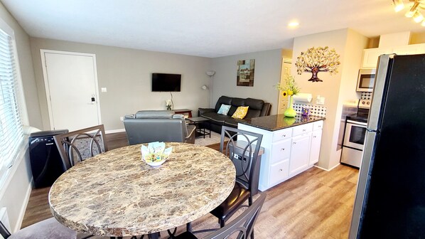 A compact kitchen with a dining area, a flat-screen TV mounted on the wall, and a refrigerator.
