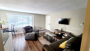 A living room with a sofa, a recliner, a coffee table, a TV, and a dining area with a table and chairs. - 2 Bedroom Single Story Townhouse (Beaverton)
