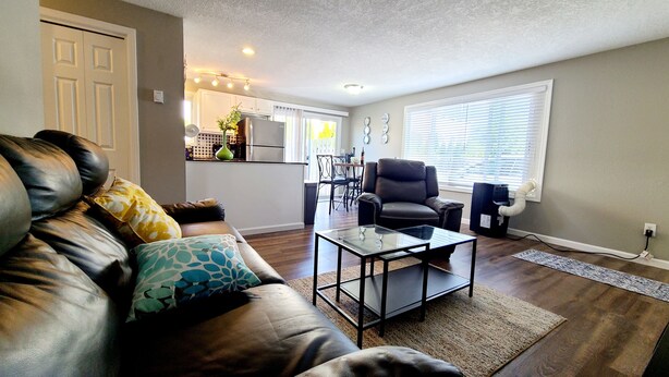 A living room with a leather couch, a glass coffee table, and a dining area in the background. - 2 Bedroom Single Story Townhouse (Beaverton)