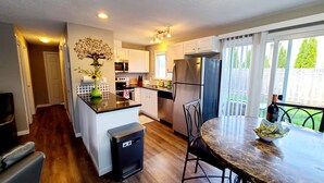 A modern kitchen with white cabinets, a stainless steel refrigerator, and a dining area with a marble table. - 2 Bedroom Single Story Townhouse (Beaverton)