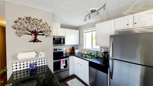 A modern kitchen with white cabinets, a stainless steel refrigerator, a microwave, and a sink. - 2 Bedroom Single Story Townhouse (Beaverton)